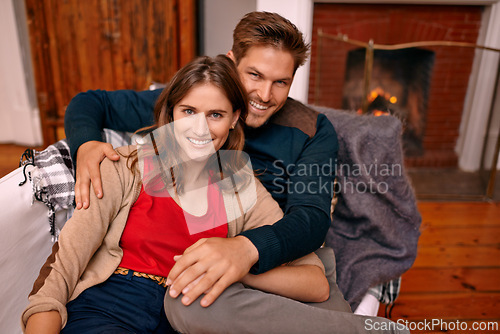 Image of Couple, portrait and together in living room for romance, partners and smile for relationship. People, happy and love for marriage in house with fireplace to keep warm in winter, sitting and hugging