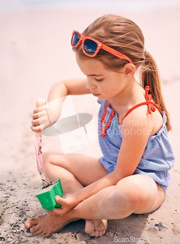 Image of Little girl, toys and playing with beach sand, castle or summer fun on outdoor holiday or weekend in nature. Female person, child or kid with scoop and shape for building sandcastle by ocean coast