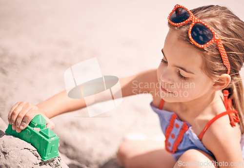 Image of Girl, toys and building sandcastle on the beach with shape or block for fun summer, holiday or weekend in nature. Female person, child or kid playing and enjoying sand construction by the ocean coast