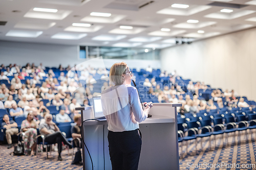 Image of Female speaker giving a talk on corporate business conference. Unrecognizable people in audience at conference hall. Business and Entrepreneurship event.