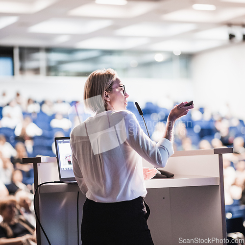 Image of Female speaker giving a talk on corporate business conference. Unrecognizable people in audience at conference hall. Business and Entrepreneurship event.