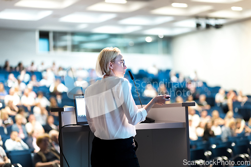 Image of Female speaker giving a talk on corporate business conference. Unrecognizable people in audience at conference hall. Business and Entrepreneurship event.