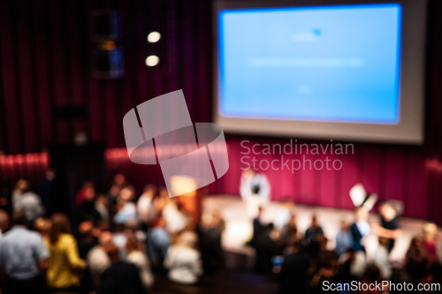 Image of Blured image of Business and entrepreneurship symposium. Female speaker giving a talk at business meeting. Audience in conference hall. Rear view of unrecognized participant in audience