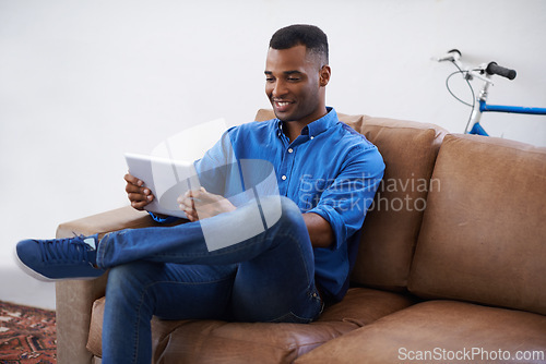 Image of Man, tablet and relax on social media at home, online and internet for website or blog. Black male person, smile and streaming entertainment on armchair, video call and app for shopping on weekend