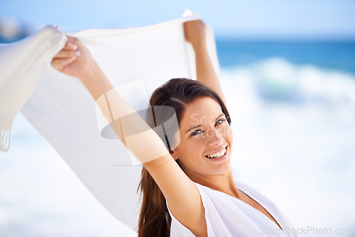 Image of Portrait, happy woman and sarong in wind at beach outdoor for summer, vacation and travel on holiday. Ocean, smile and person fly with fabric in the air for freedom, breeze and face by water in Spain