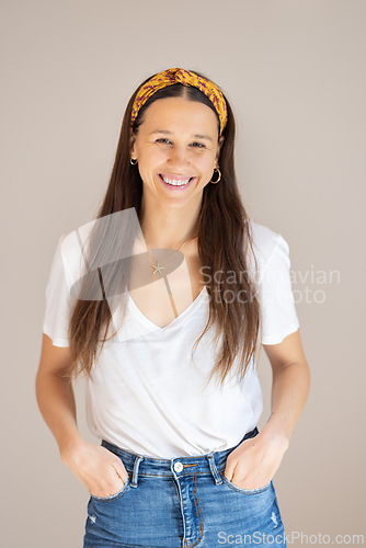 Image of Portrait of confident beautiful woman with long brown hair, wearing casual clothes, standing in relaxed pose with hands in pockets, smiling with white teeth at camera, studio background.