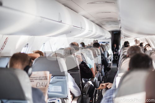 Image of Interior of airplane with passengers on seats and stewardess in uniform walking the aisle, serving people. Commercial economy flight service concept.