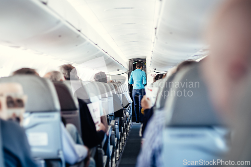 Image of Interior of airplane with passengers on seats and stewardess in uniform walking the aisle, serving people. Commercial economy flight service concept.