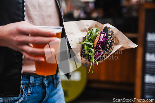 Image of Close up of woman hands holding delicious organic salmon vegetarian burger and homebrewed IPA beer on open air beer an burger urban street food festival in Ljubljana, Slovenia.