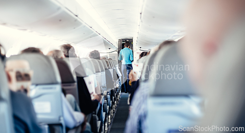 Image of Interior of airplane with passengers on seats and stewardess in uniform walking the aisle, serving people. Commercial economy flight service concept.