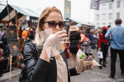 Image of Beautiful young woman holding delicious organic salmon vegetarian burger and drinking homebrewed IPA beer on open air beer an burger urban street food festival in Ljubljana, Slovenia.