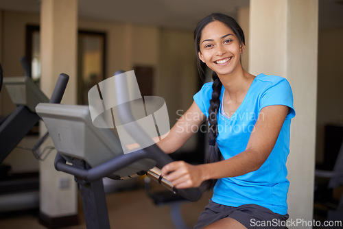 Image of Woman, portrait and exercise bike in gym, cycling and stationary machine for workout at club. Female person, cardio and cycling for strength training, smile and equipment for fitness and health