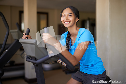 Image of Woman, portrait and workout bike in gym, cycling and stationary machine for exercise or training. Happy female person, cardio and cycling for wellness, smile and equipment for fitness and health