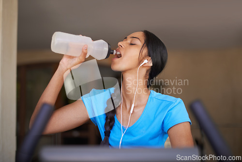 Image of Woman, water and exercise bike in gym, cycling and stationary machine for workout at club. Female person, earphones and hydrate for strength training, music and equipment for fitness and body health