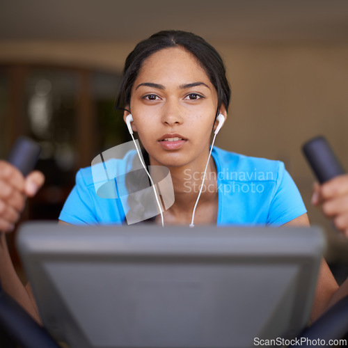 Image of Woman, earphones and cycling in portrait, bike and stationary machine for workout at club. Female person, cardio and podcast or sound and audio, playlist and equipment for fitness and body health