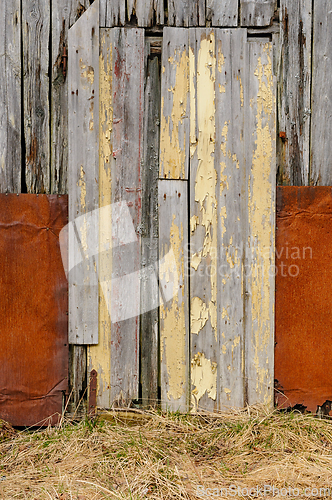 Image of Weathered wooden door with peeling yellow paint on a rustic barn