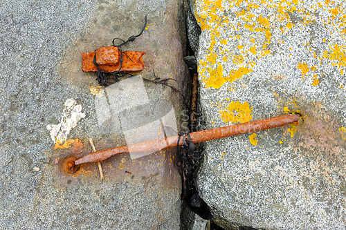 Image of Rusty metal anchor secured in weathered stone pier by the sea
