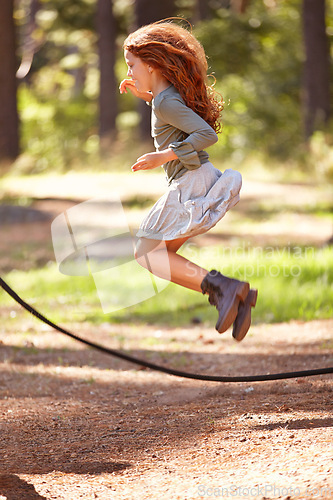 Image of Jump, rope and girl outdoor for game in forest, park or playing on summer, holiday and vacation. Child, skipping and energy for fun activity in nature with trees in backyard or garden with kid in air