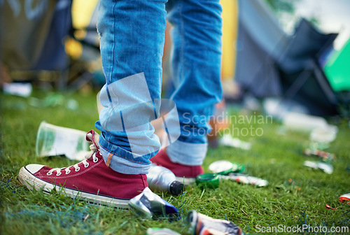 Image of Feet, event and a person with litter on grass and plastic bottles, cans at an outdoor festival. People at a party, concert with garbage on a field and shoes with pollution for recycling trash