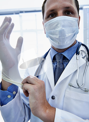 Image of Portrait, doctor and man putting on gloves for safety or protection in hospital. Face mask, medical professional or ppe to prepare for surgery, treatment or prevention of disease in healthcare clinic