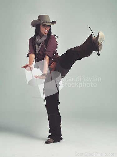 Image of Western, woman and cowboy in studio with fashion, leg up and gesture to fight on grey background. Female person, vintage and outlaw with boots for wild west, costume and character with retro hat