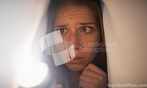 Image of Flashlight, scared and woman with blanket on bed with anxiety, stress or risk for mystery. Torch, fear and young female person with duvet for protection of horror, terror or danger with panic.