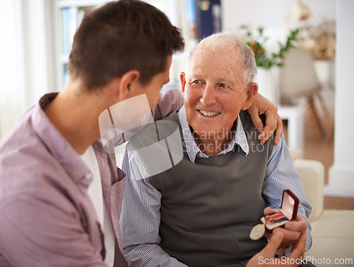 Image of Father, adult son and medal for gift, support and congratulations with celebration and bonding at home. Men in living room, family time with reward or award for present, happiness and gratitude