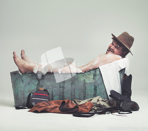 Image of Cowboy, studio and bathtub with comic bandit, naughty and plus size man on white background. Retro, wild west and male model in metal tub, grin and smoking cigar while bathing with mockup space