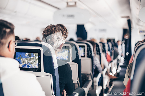 Image of Interior of airplane with passengers on seats and stewardess in uniform walking the aisle, serving people. Commercial economy flight service concept.