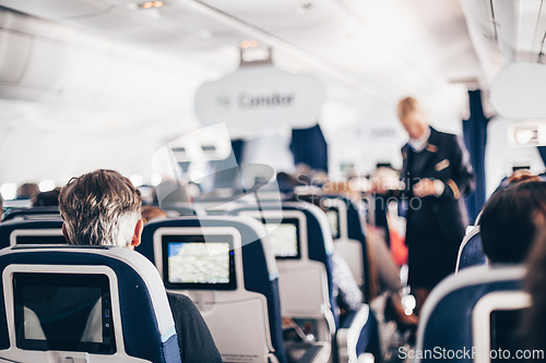 Image of Interior of airplane with passengers on seats and stewardess in uniform walking the aisle, serving people. Commercial economy flight service concept.