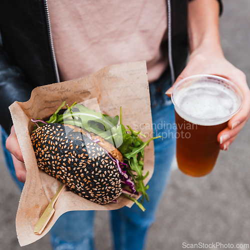 Image of Close up of woman hands holding delicious organic salmon vegetarian burger and homebrewed IPA beer on open air beer an burger urban street food festival in Ljubljana, Slovenia.