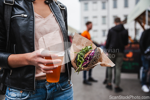 Image of Close up of woman hands holding delicious organic salmon vegetarian burger and homebrewed IPA beer on open air beer an burger urban street food festival in Ljubljana, Slovenia.