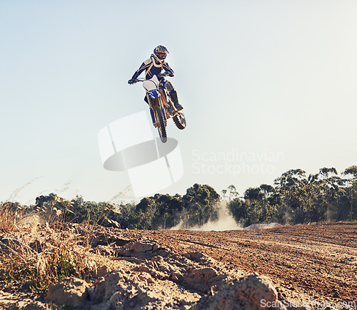 Image of Person, jump and motorbike of professional motorcyclist in the air for trick, stunt or race on outdoor dirt track. Expert rider on bike or scrambler in dunes or extreme sport with blue sky background