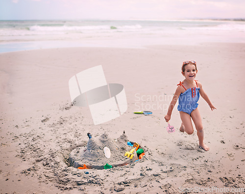 Image of Portrait, beach and little girl running with sandcastle outdoor by sea or ocean for carefree fun. Nature, water and energy with happy young child playing on sand at coast for holiday or vacation