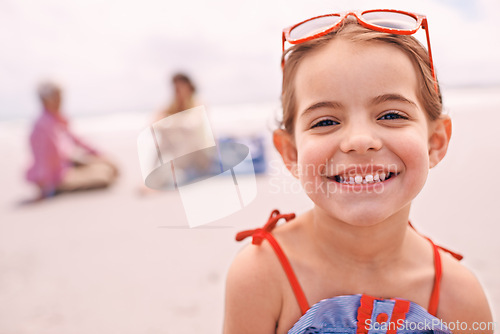 Image of Portrait, relax and little girl on beach in summer with family for travel, holiday or vacation. Face, smile and sunshine with happy young child on sand by ocean or sea for tropical weekend getaway