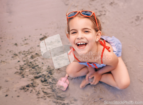 Image of Happy, portrait and little girl playing with sand at the beach for fun holiday, weekend or summer. Face of female person, child or kid with smile in happiness for day by the sandy shore in nature