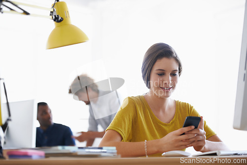 Image of Woman, smartphone and online at desk, smiling at device for notification.Digital, technical career and creative web design with happy employee, scrolling and browsing internet on social media