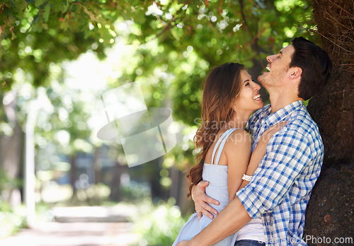 Image of Young couple, laughing and hug with love under the trees in the park and enjoying sunshine views in the summer sun. Cheerful, affection outdoor and romantic partners bonding with a nature lifestyle