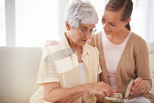 Image of Mother, old woman and adult daughter with pearl necklace, home and conversation in a lounge. Family, pensioner and girl on a couch, relaxing and discussion with jewelry, present and gift for birthday