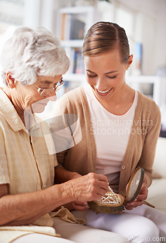 Image of Mother, elderly woman and daughter with pearl necklace, home and conversation in a living room. Family, old lady and adult on a couch, relaxing and discussion with jewelry, present or inheritance