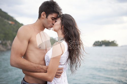 Image of Summer, holiday and couple kiss by sea in vacation, water and outdoor for date in nature for romance. Partners, woman and man together to travel, journey and adventure in ocean for love with hug