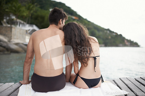 Image of Couple, jetty and travel to ocean on vacation, touch and relax by water on summer holiday. People, swimwear and bonding for relationship in outdoors, support and back on weekend trip to sea or nature