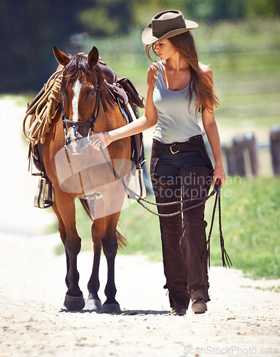 Image of Woman, cowgirl and walking with horse in the countryside for outdoor ride on the farm in nature. Female person or western rider with hat, saddle and animal or stallion at ranch for mount by the field