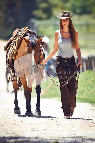 Image of Woman, portrait and cowgirl walking with horse in countryside for ride, journey or outdoor adventure in nature. Female person or western rider with hat, saddle and animal stallion at ranch or farm