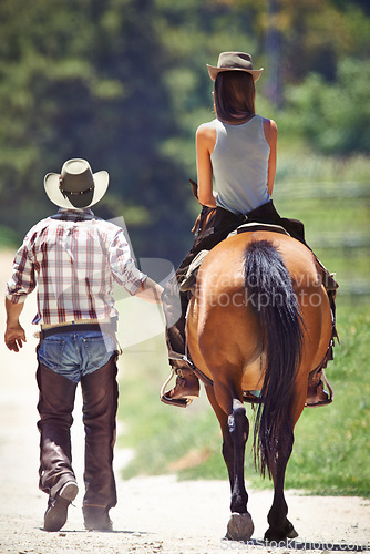 Image of Back of woman, cowboy or horse riding on countryside farm as equestrian for training, sport or learning. Walking, teaching or people in Texas, outdoor environment or stable for practice on saddle