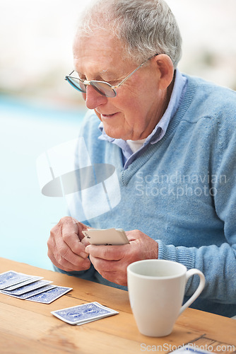 Image of Elderly man, coffee and playing cards on table for poker, relax and happy in retirement. Senior person, grandfather and beverage with thinking, hobby and fun strategy on patio in home drinking tea