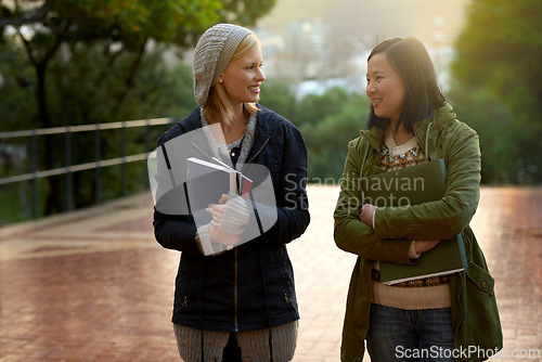 Image of Students, women and friends on campus for university, conversation while walking to class and smile outdoor. College, communication and books for studying, education and academic growth with talk