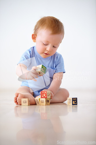 Image of Baby boy, wooden blocks and playing with toys in early childhood development on a gray studio background. Little toddler or child on floor with shape or cube in building, learning or cognitive skills