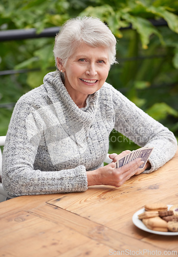 Image of Elderly woman, cookies and portrait with cards at table for relaxation, old age and retirement. Senior person or grandmother and smiling with wrinkles for poker game, gamble and hobby for leisure