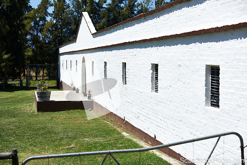 Image of Horse stable, building and wall on farm with nature, trees and grass on countryside. Plot landscape, window and gate with fence shed, brick or plants and lawn in outdoor or farmland or western